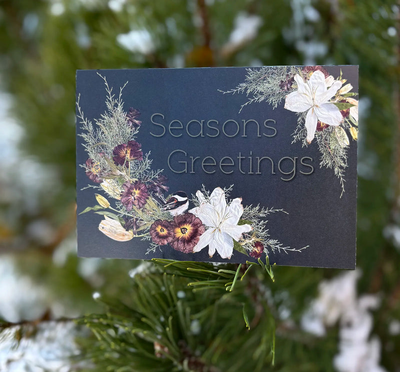 Seasons Greetings card with floral design on a snowy tree background