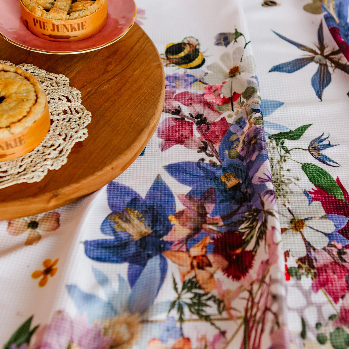 Two pies on a wooden stand with floral tea towel in the foreground