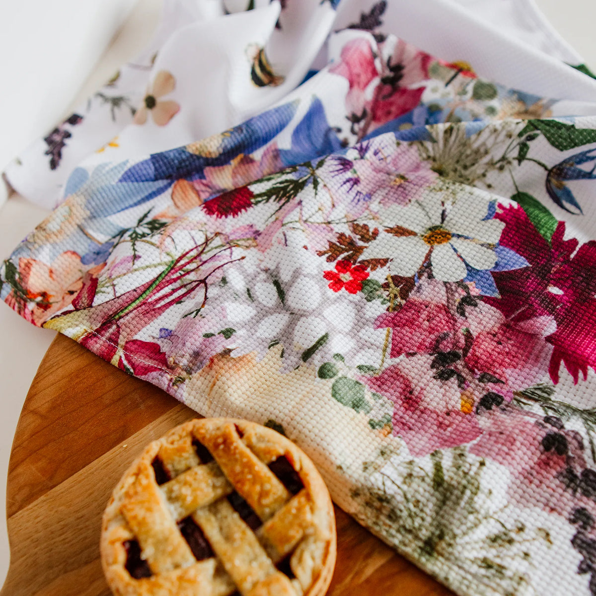 Floral-patterned kitchen towel with a small pie on a wooden board