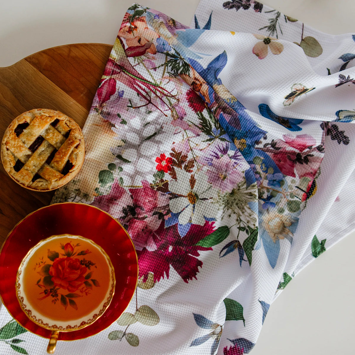Decorative pressed flower tea towel with a pie and teacup on a wooden surface