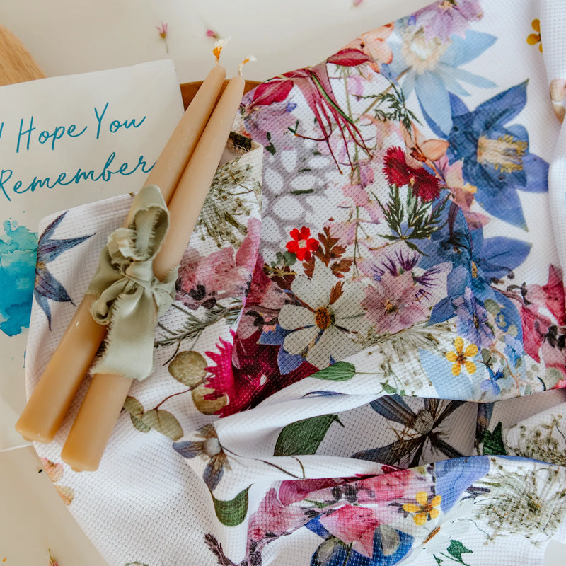 Floral-patterned tea towel with two beeswax candles on a white background