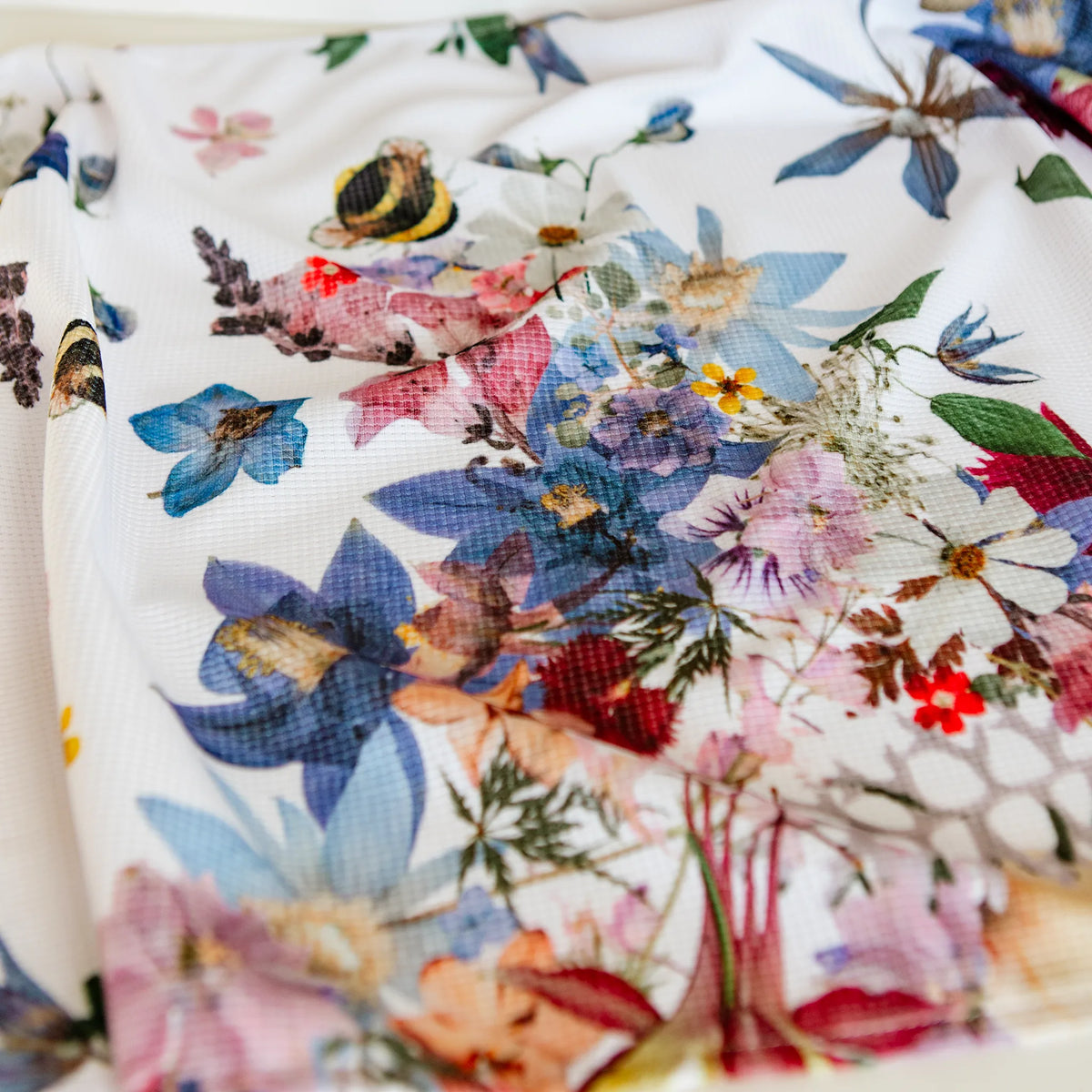 Floral and bumblebee patterned tea towel with colorful pressed flowers on a white background