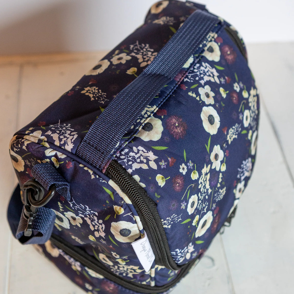 Dark pressed flower soft-shell cooler bag on a neutral wood background