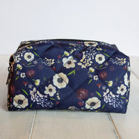 Floral-patterned quilted clutch bag on a light wooden surface