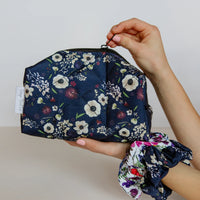 Navy floral pouch held by a hand with matching scrunchie on a neutral background