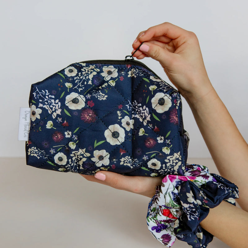 Navy floral pouch held by a hand with matching scrunchie on a neutral background
