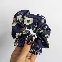 Navy blue floral scrunchie held by a hand on a light gray background