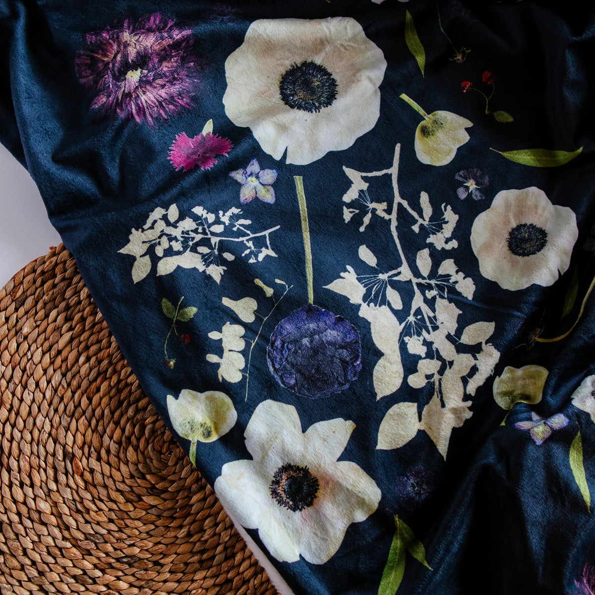 Pressed flower patterned blanket with white flowers on a dark blue background, draped over a woven surface.