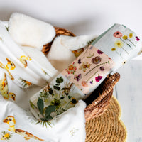 Rolled up baby swaddle with floral design on top of a duck-themed baby blanket in a wicker basket