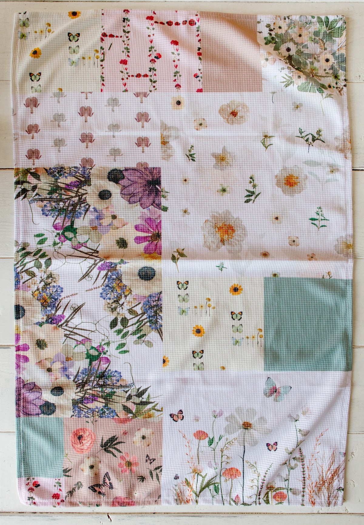 Patchwork quilt style tea towel with floral and butterfly patterns on a wooden surface