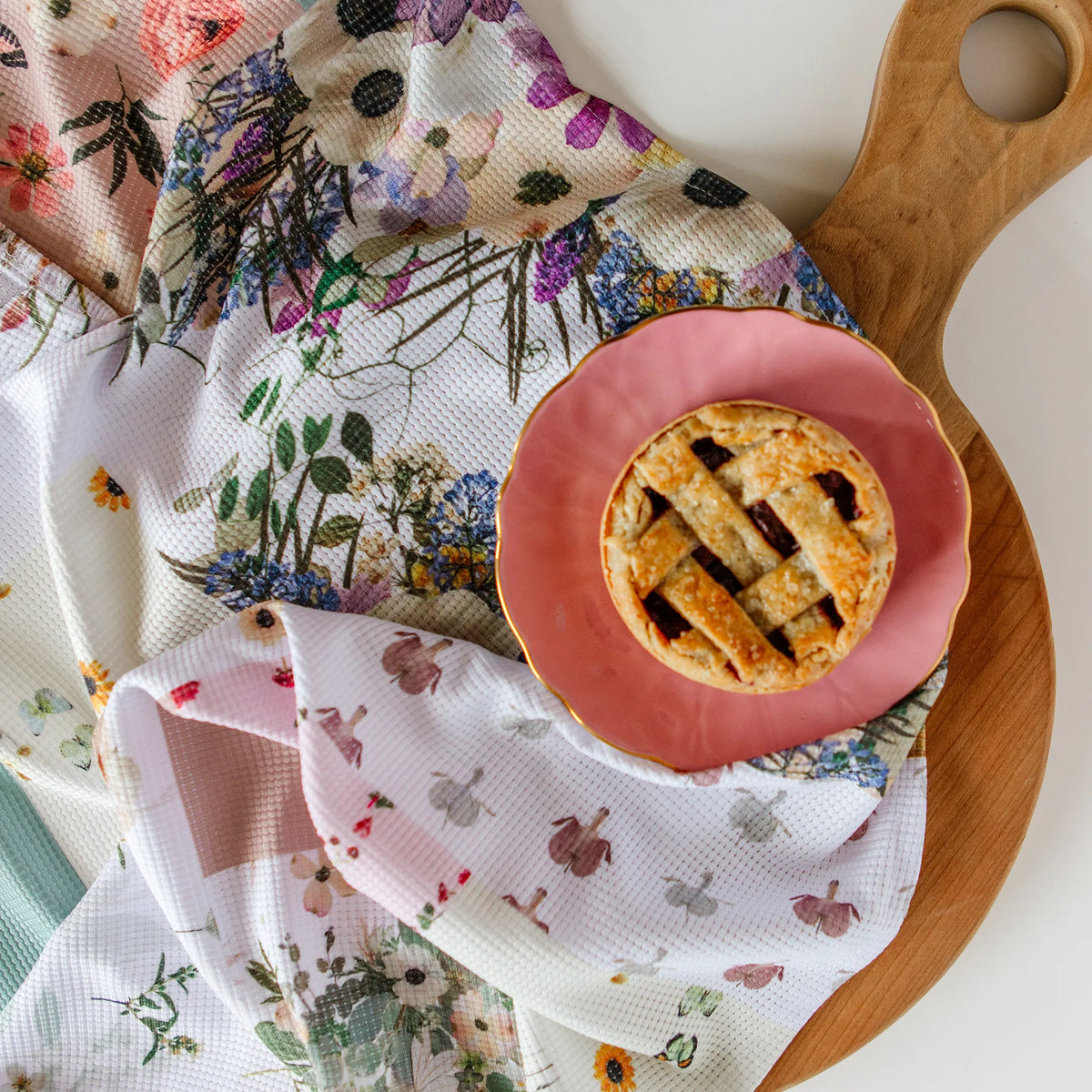 Small pie on a pink plate with floral and patterned towel underneath