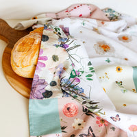 Floral patterned tea towel draped over bread on a wooden board