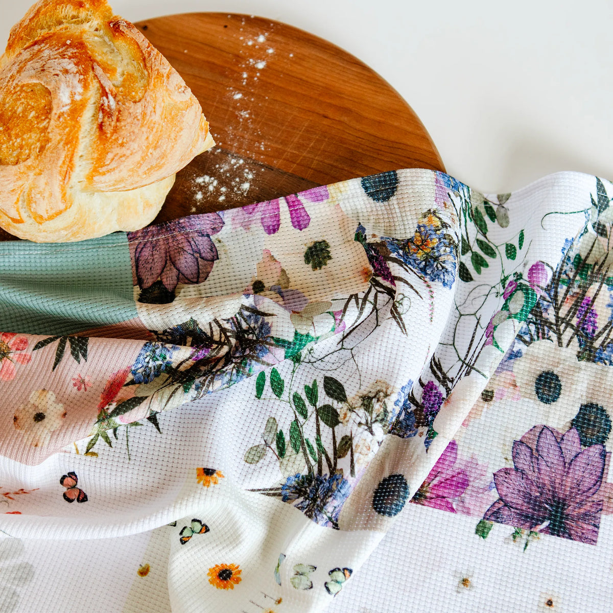 Floral tea towel with patchwork style print on a cutting board with fresh bread