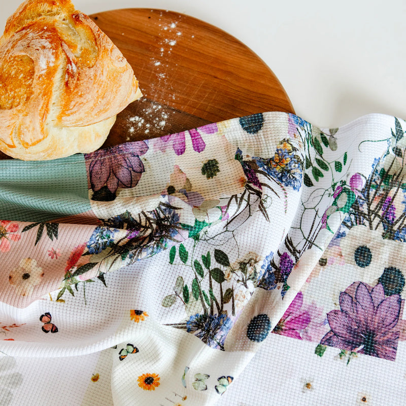 Floral tea towel with patchwork style print on a cutting board with fresh bread