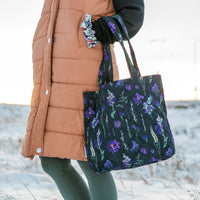 Woman holding a black and purple floral tote bag outdoors in the snow