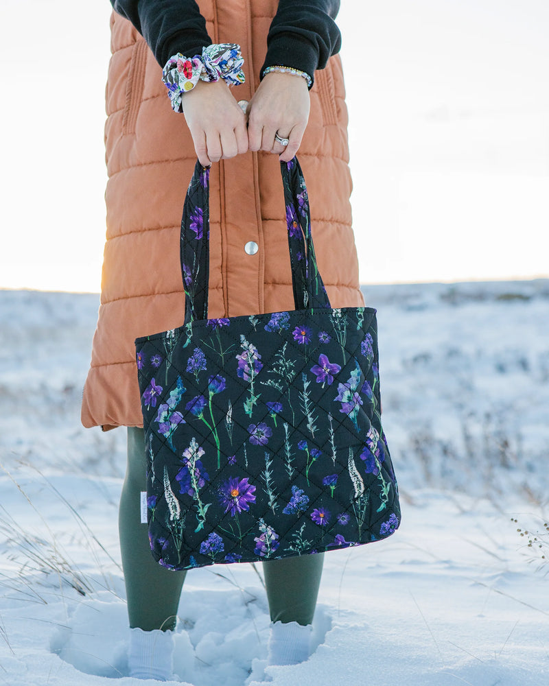 Woman holding  black and purple floral tote bag outside in the snow