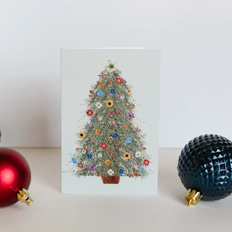 Card with a floral Christmas tree design, surrounded by festive ornaments on a light background