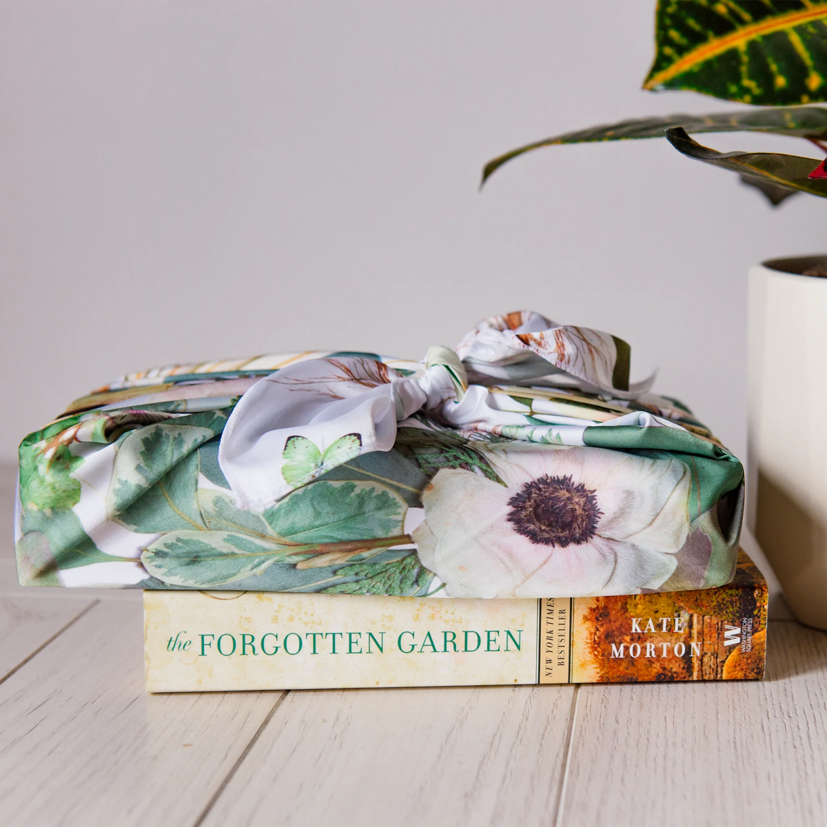 Pressed flower themed reusable gift wrapping fabric on top of a book next to a plant