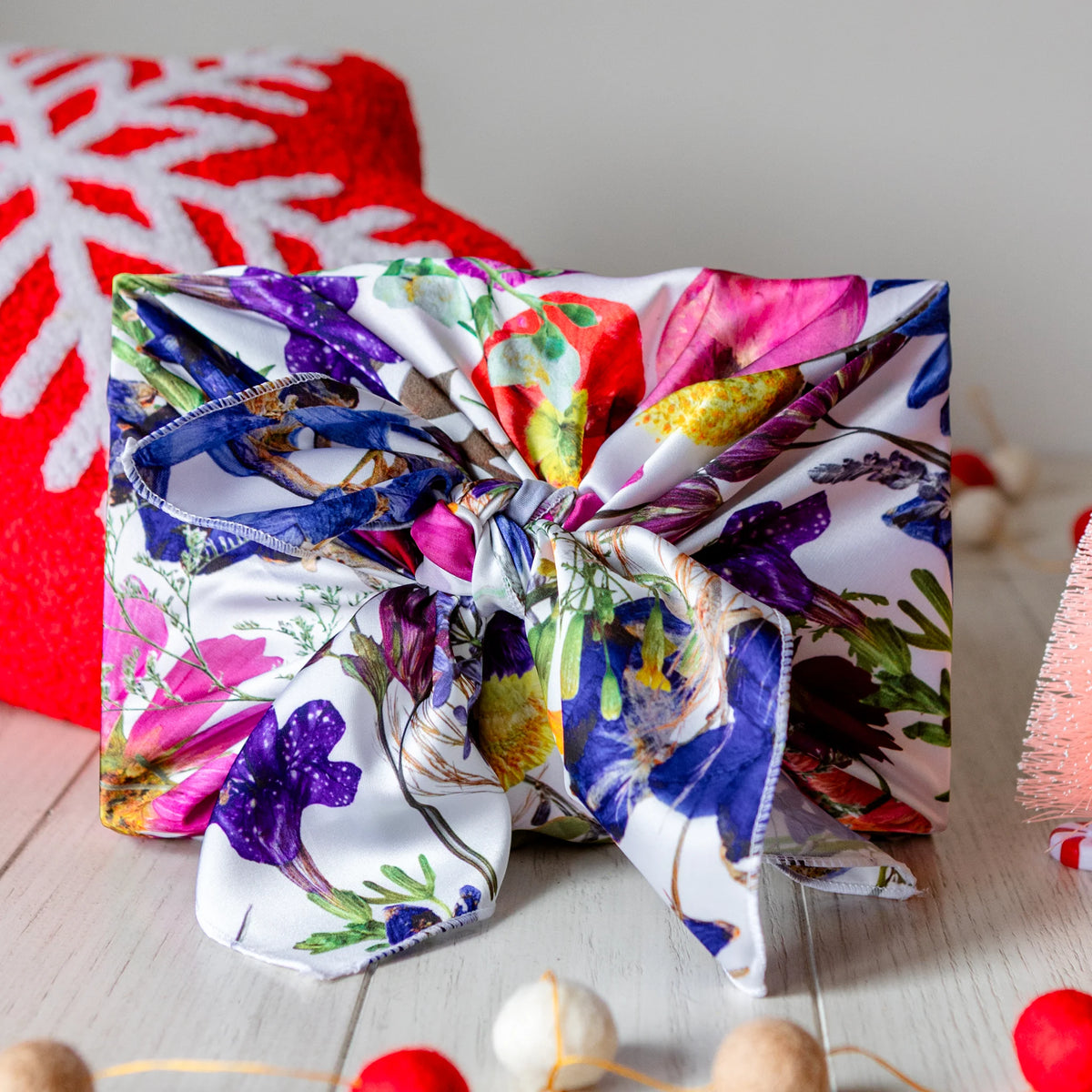 Gift wrapped in faux silk reusable floral gift wrap with christmas decoration around it.