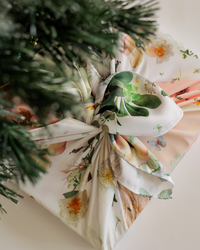 Gift under a tree wrapped in reusable fabric wrap with pressed flower design